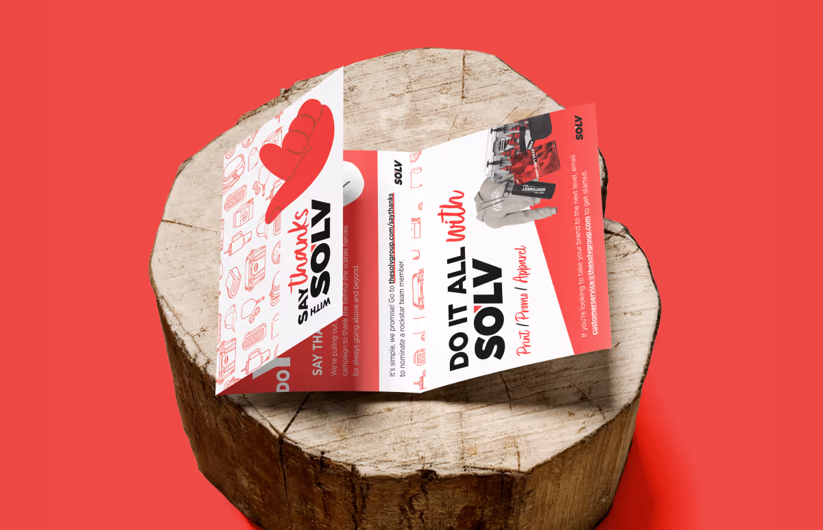 Two red and white folded brochures placed on a tree stump against a red background. The brochures feature text and images related to SOLV, with a playful and inviting design.