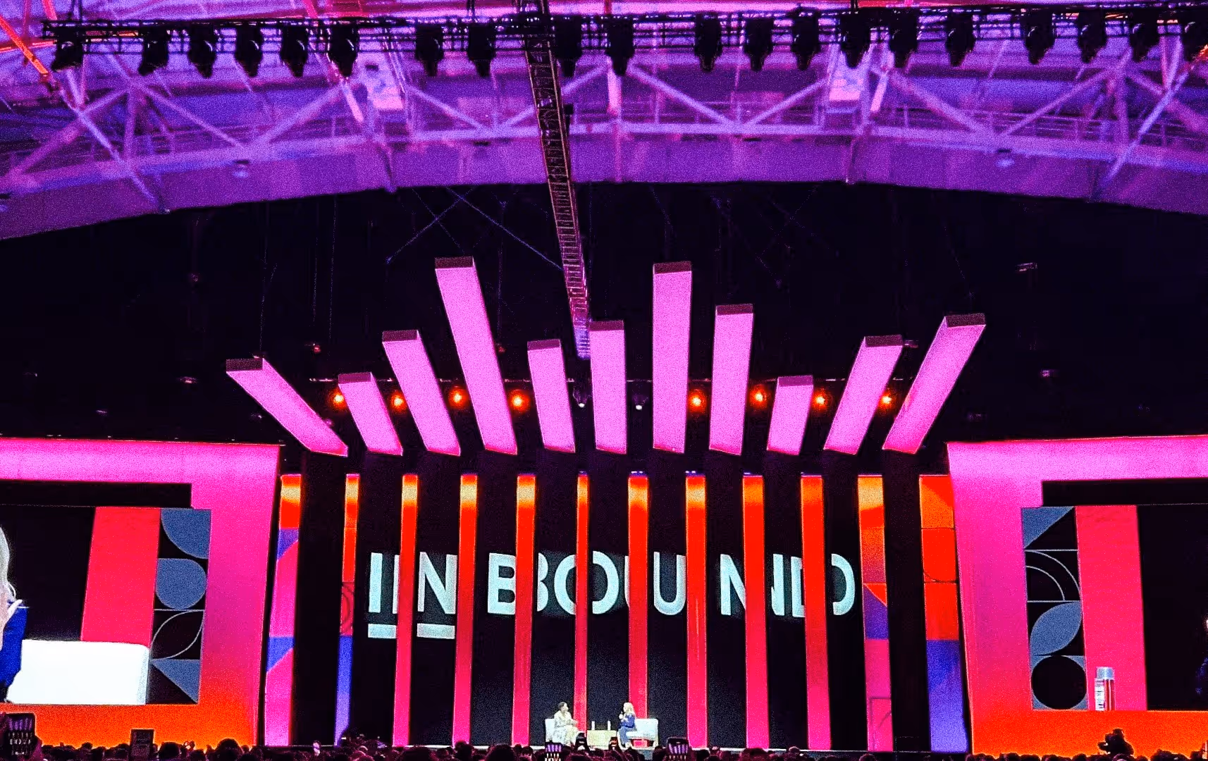 A vibrant stage setup at a conference with the word "INBOUND" in bold letters. Two speakers sit in conversation under dynamic, multicolored lights.