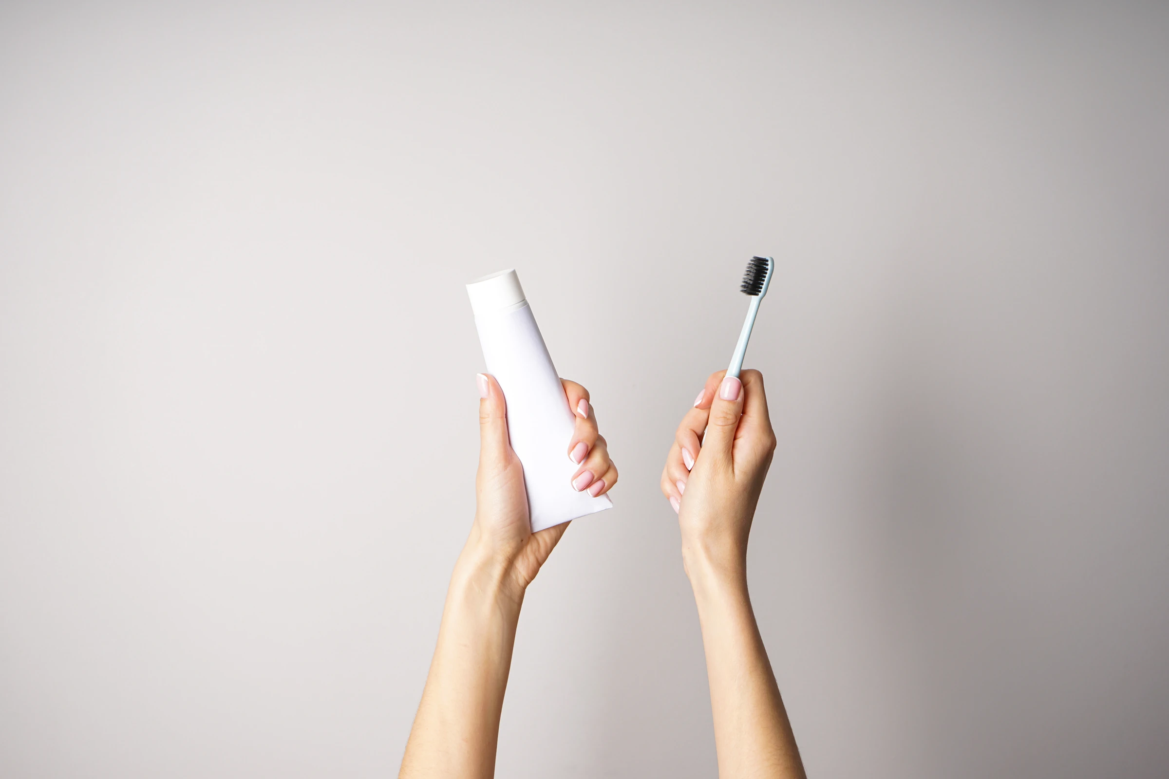 Image of someone holding a toothbrush and toothpaste in the air
