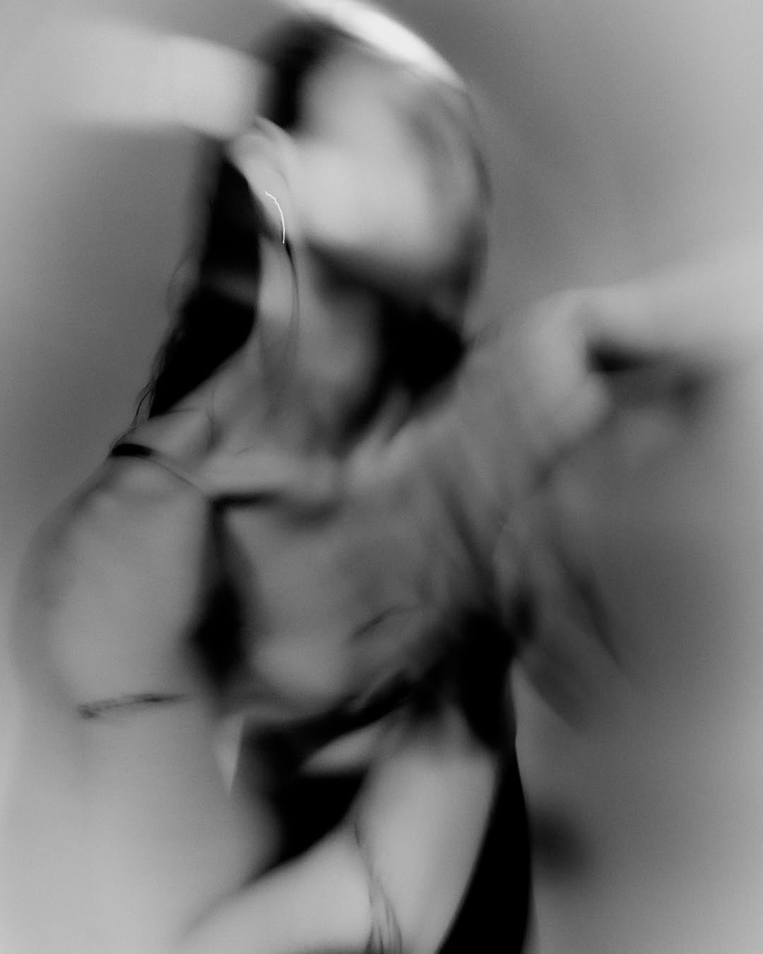 Portrait artistique en noir et blanc d'une femme floue avec la tête inclinée en arrière, portant des boucles d'oreilles et un haut à fines bretelles.