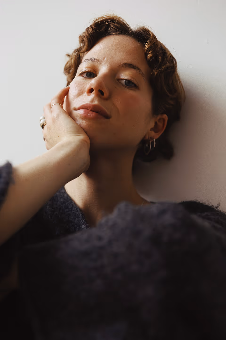 Margot Blondin accotée au mur avec une laine mauve et les cheveux courts.