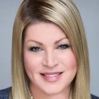 Portrait of a smiling woman with straight blonde hair and blue eyes against a gray background.
