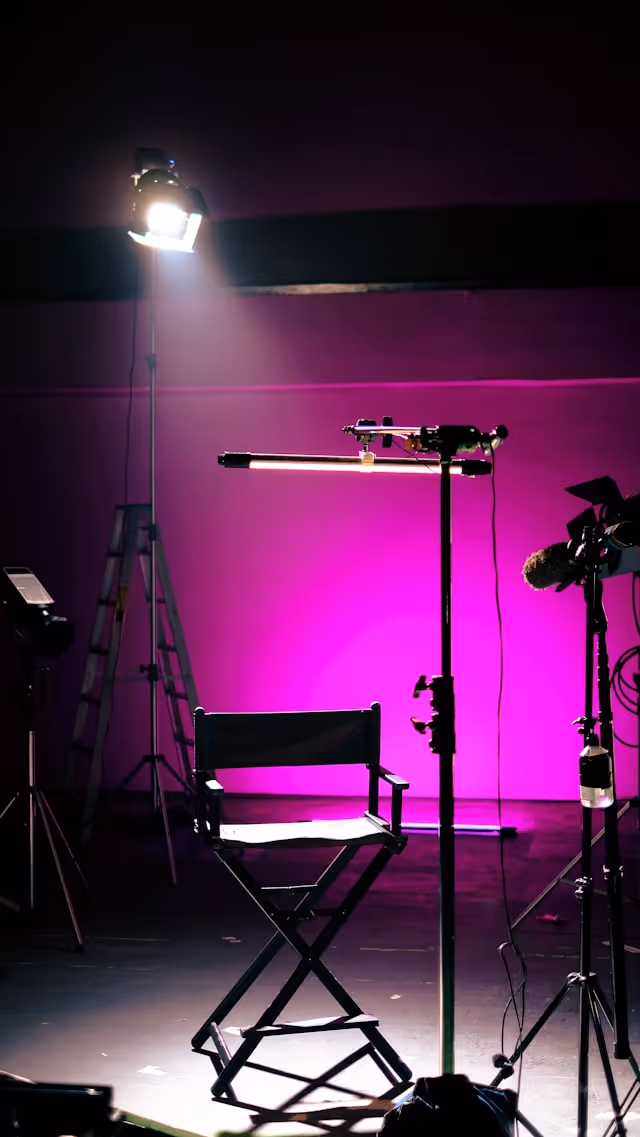 Black director's chair illuminated on a stage with a purple background and studio lighting equipment.