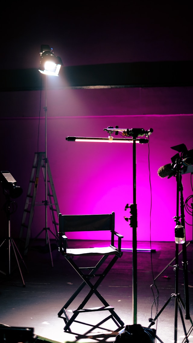 Black director's chair illuminated on a stage with a purple background and studio lighting equipment.