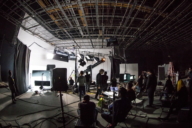 Film or photo shoot set with crew members, lighting equipment, cameras, and monitors in a dark studio.