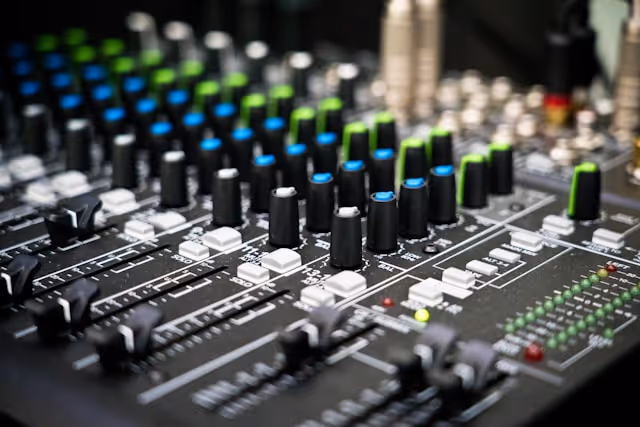 Close-up of an audio mixing console with sliders, knobs, and LED level meters.