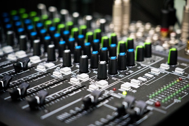 Close-up of an audio mixing console with sliders, knobs, and LED level meters.