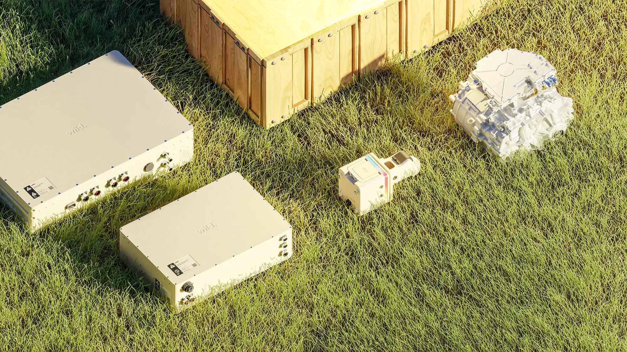 A top-down view of the Wild Trailer's internal components (power box, magic hitch, motor and battery) on a patch of grass, bathed in sunlight.