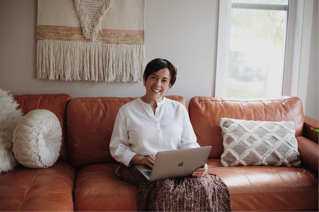 An active older woman smiles with her laptop on a couch