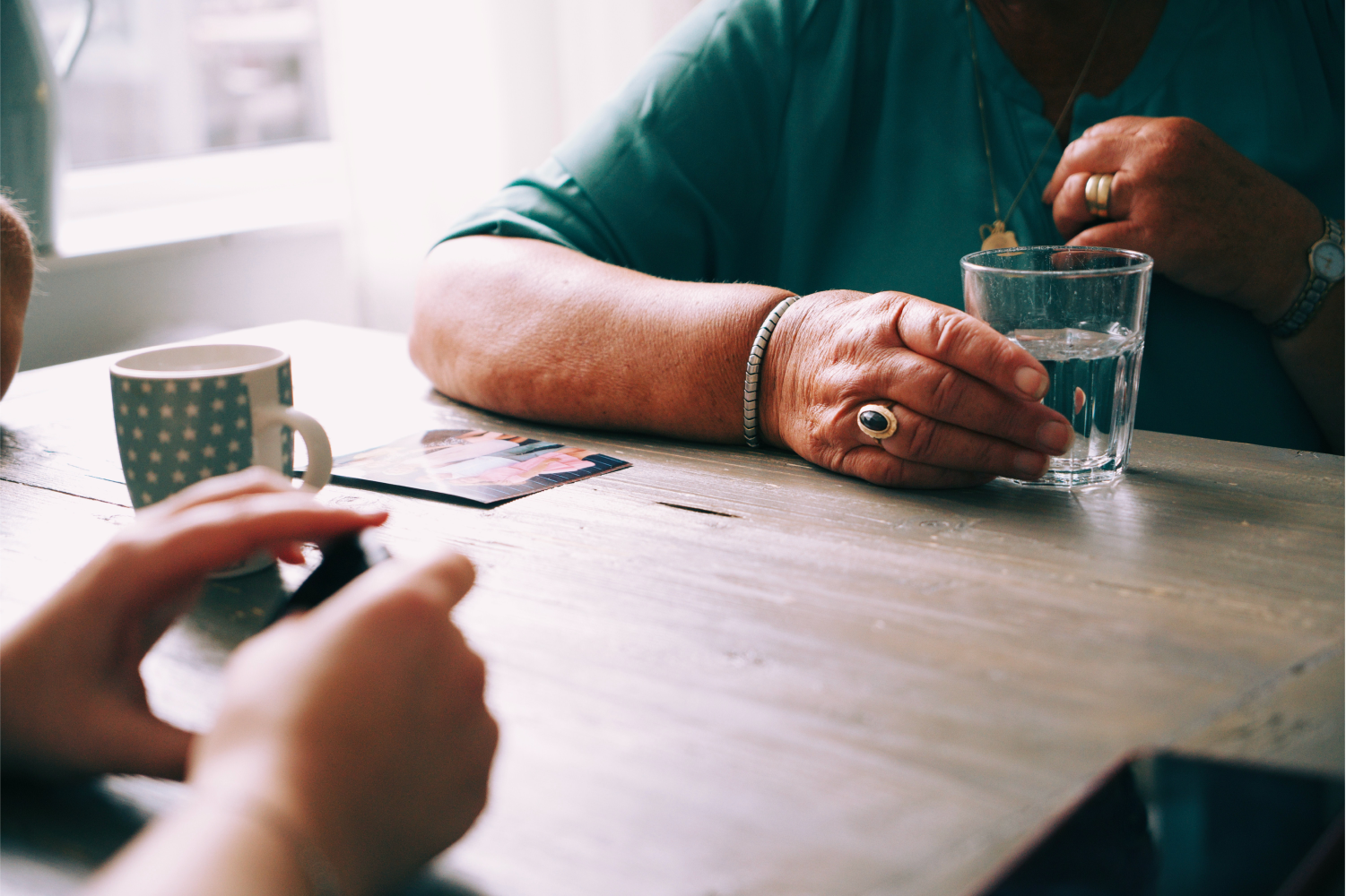 An old person and a young person play cards over a wooden table.
