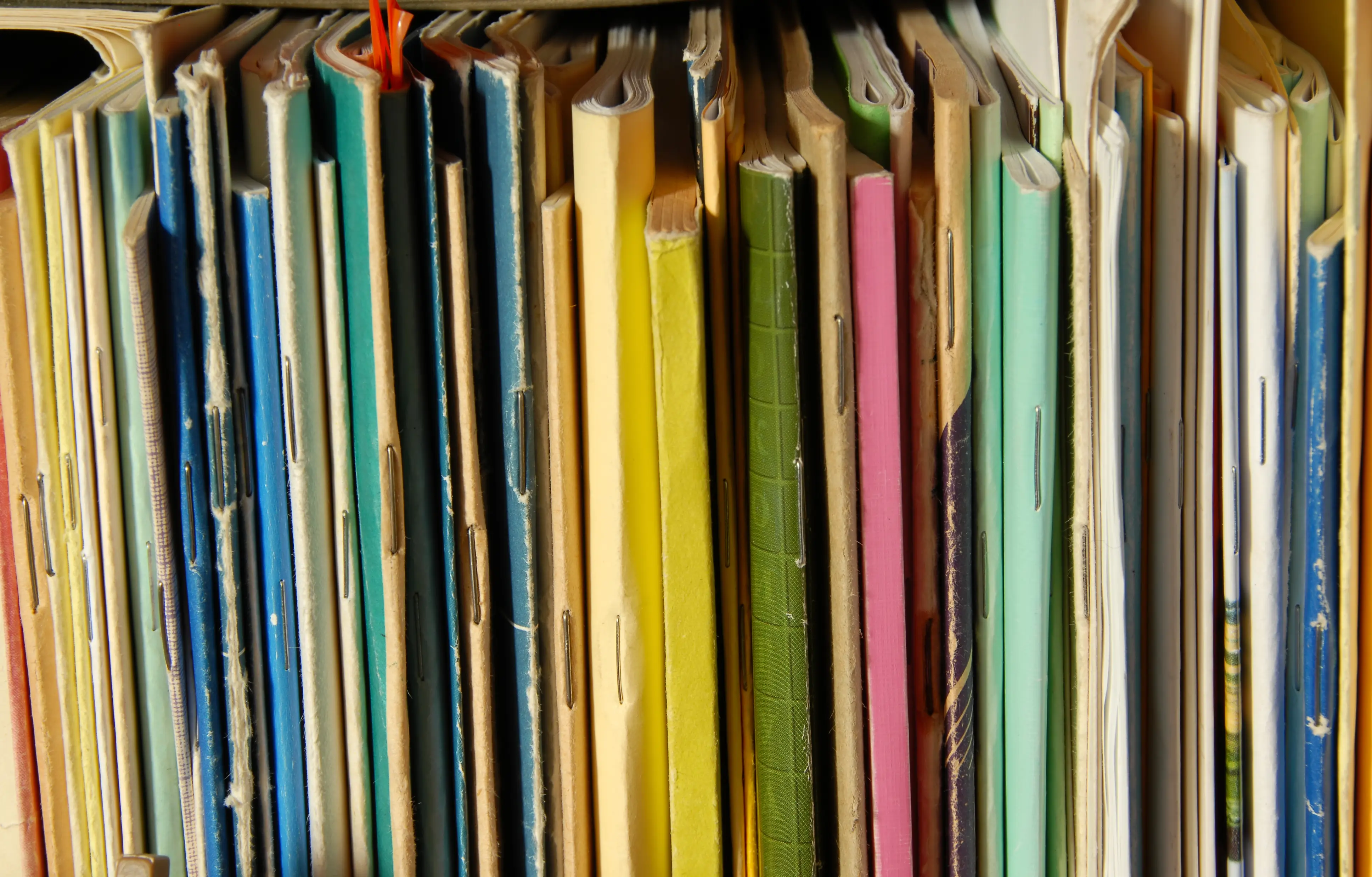 A shelf of well-used paper lab notebooks in various colors, representing legacy paper-based research documentation.