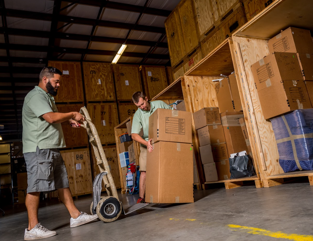 Professional movers stacking cardboard boxes onto a hand truck in a secure storage warehouse