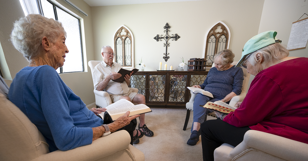 Four people in armchairs reading books in a room with a wrought-iron wall cross