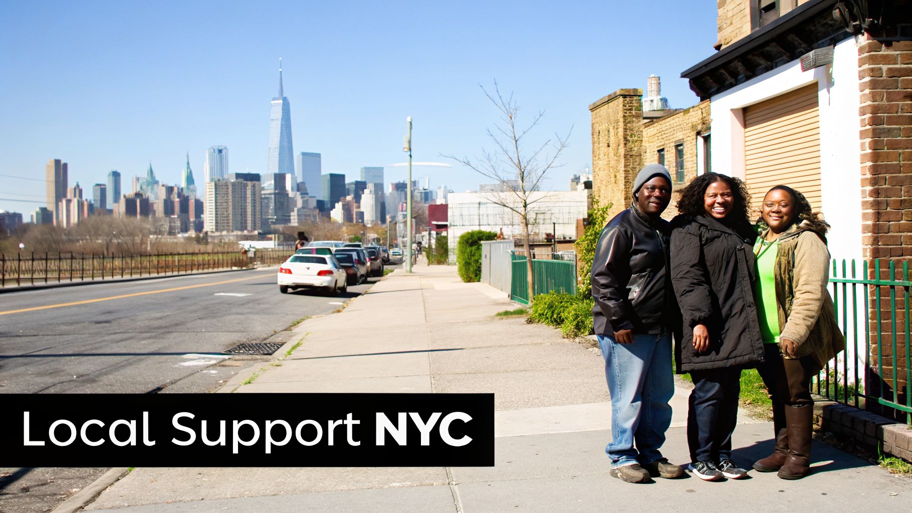 Three smiling people standing on a city sidewalk with the New York City skyline in the background.