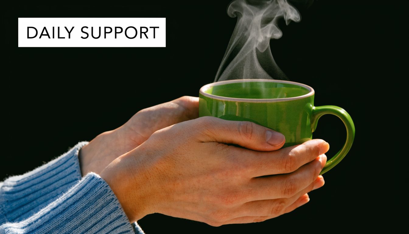 A person wearing a blue sweater holding a steaming green mug in their hands against a dark background.