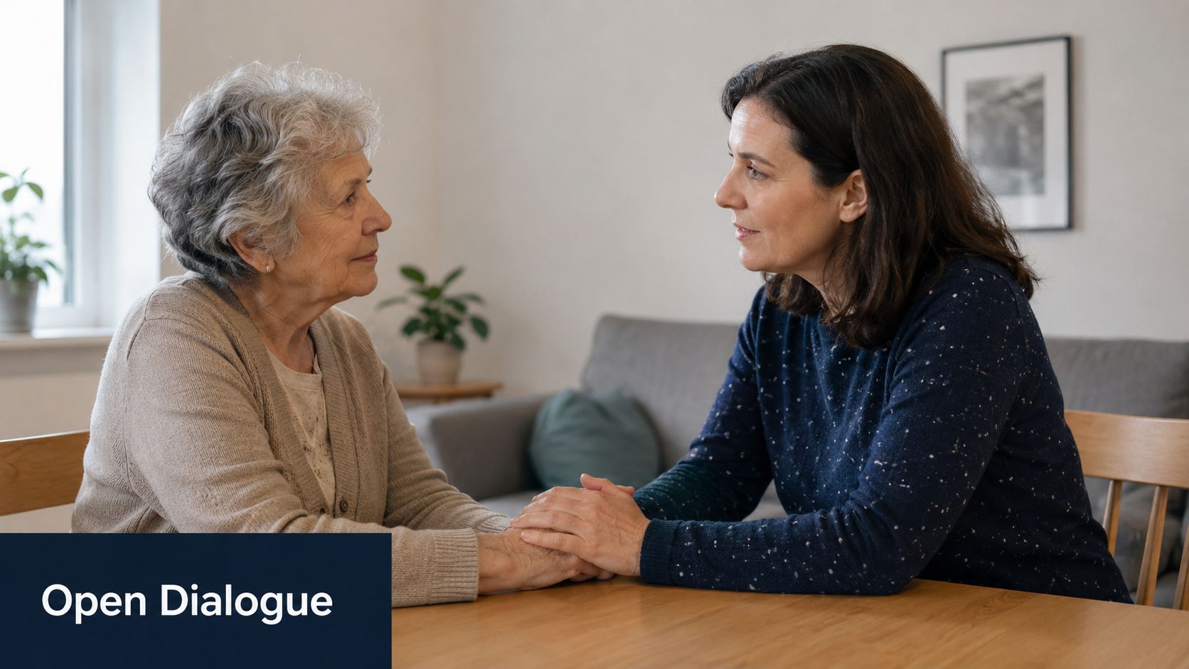 A caring adult woman holds the hands of an elderly woman while having a supportive, empathetic conversation.