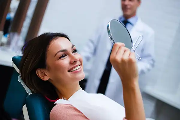 Patient in dental chair holding a mirror with dentist standing in the background.