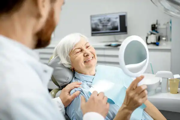 older woman in dental chair holding a mirror
