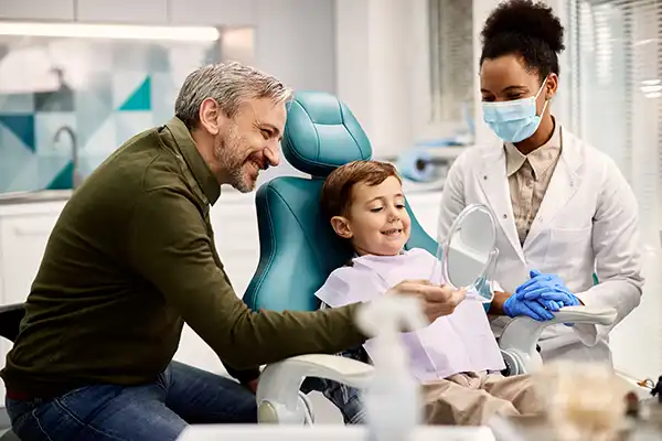 doctor and parent stand over a child at the dentist