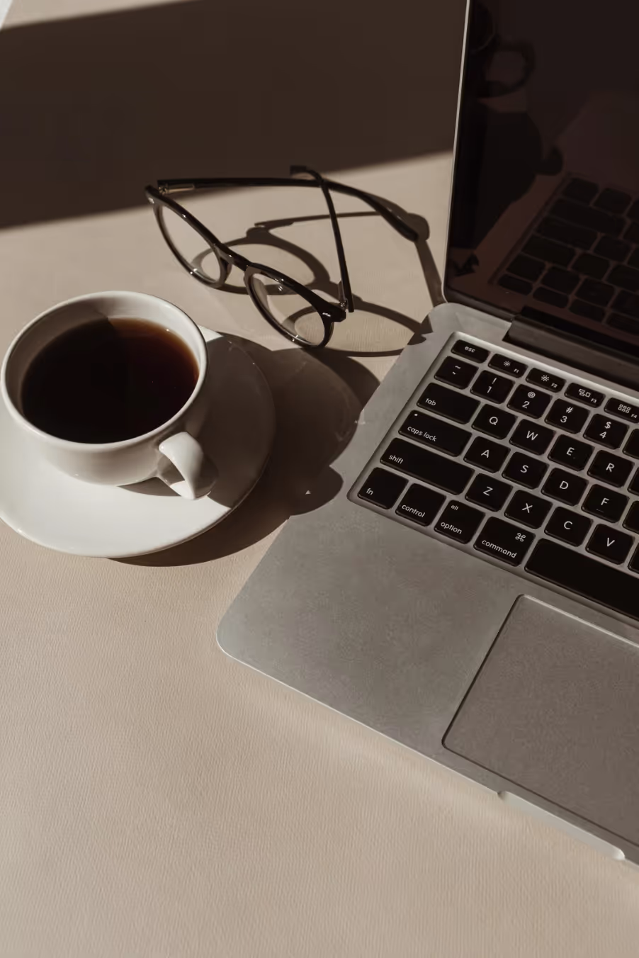 Apple laptop, glasses, and coffee cup with saucer.