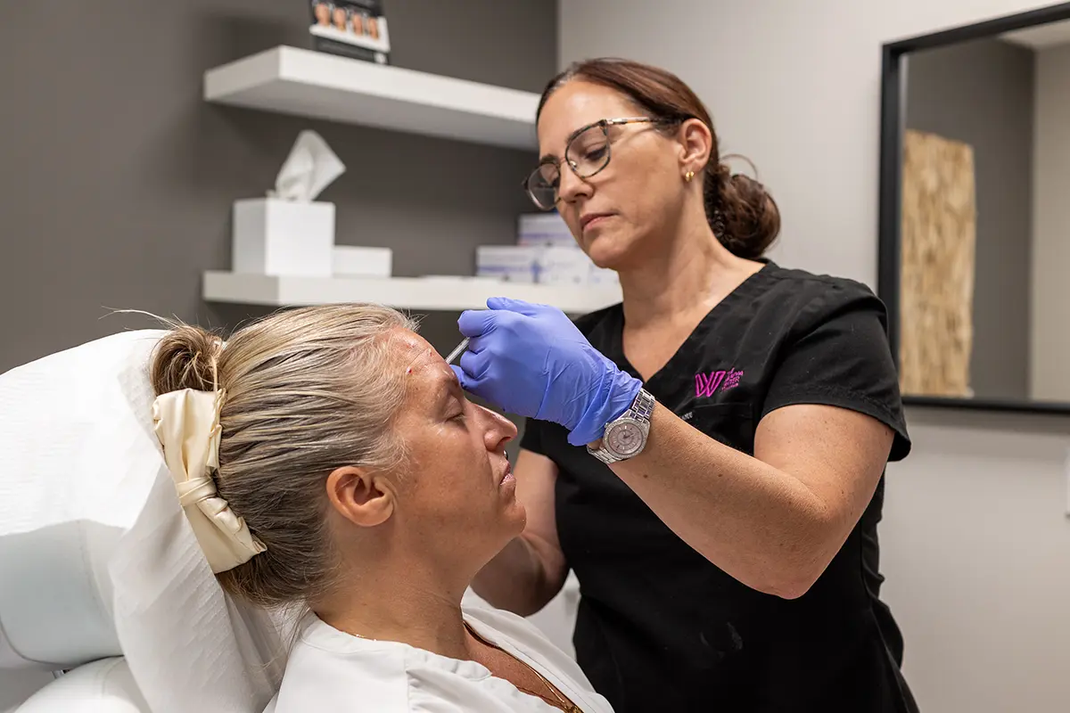 Middle-aged woman receiving injectable Botox treatment in her forehead, treating horizontal forehead lines. 