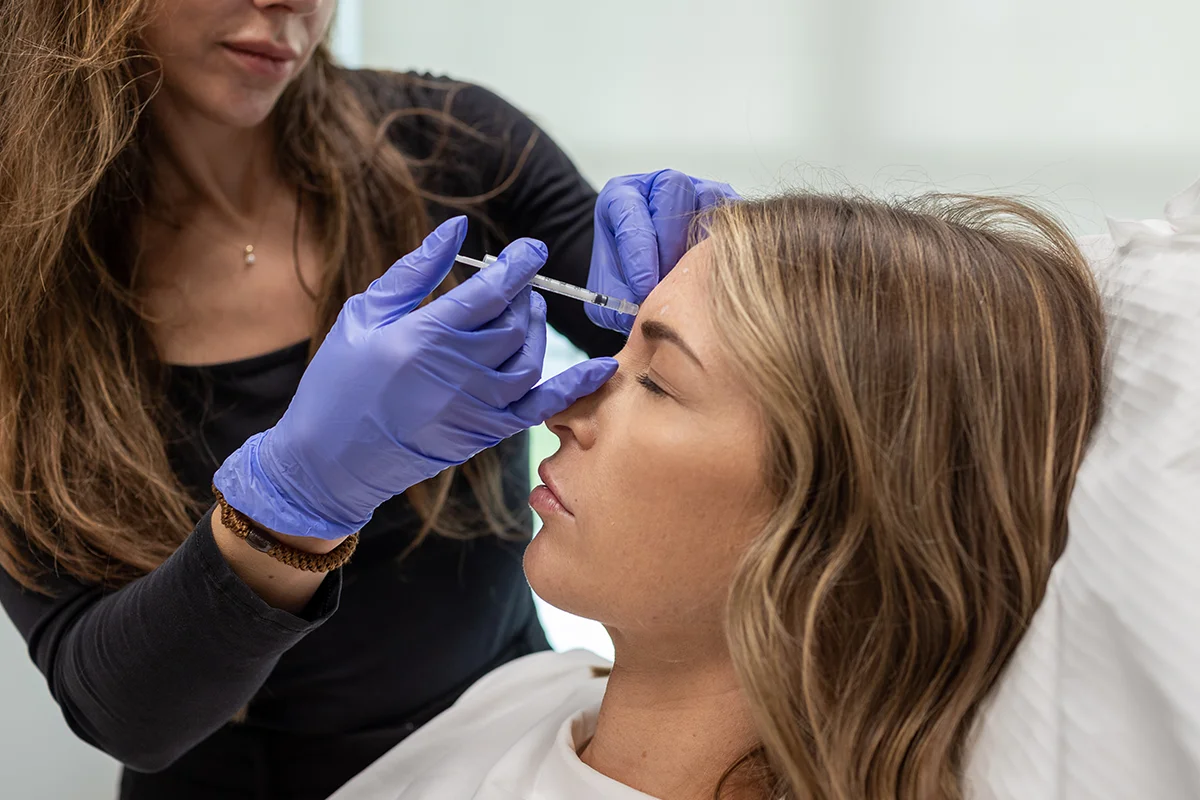 Young woman receiving injectable Daxxify treatment in between her eyebrows, treating 'frown lines.'
