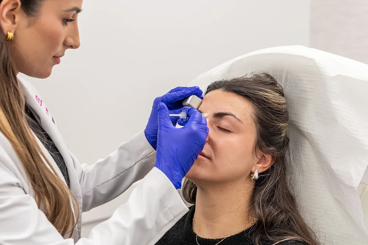 Young woman receiving injectable Daxxify treatment in between her eyebrows, treating 'frown lines.'