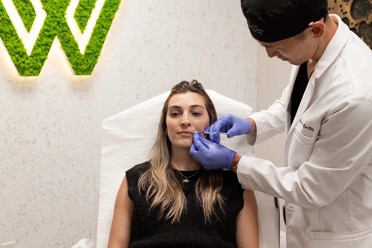 Young woman receiving injectable dermal filler in her lips for volume enhancement.