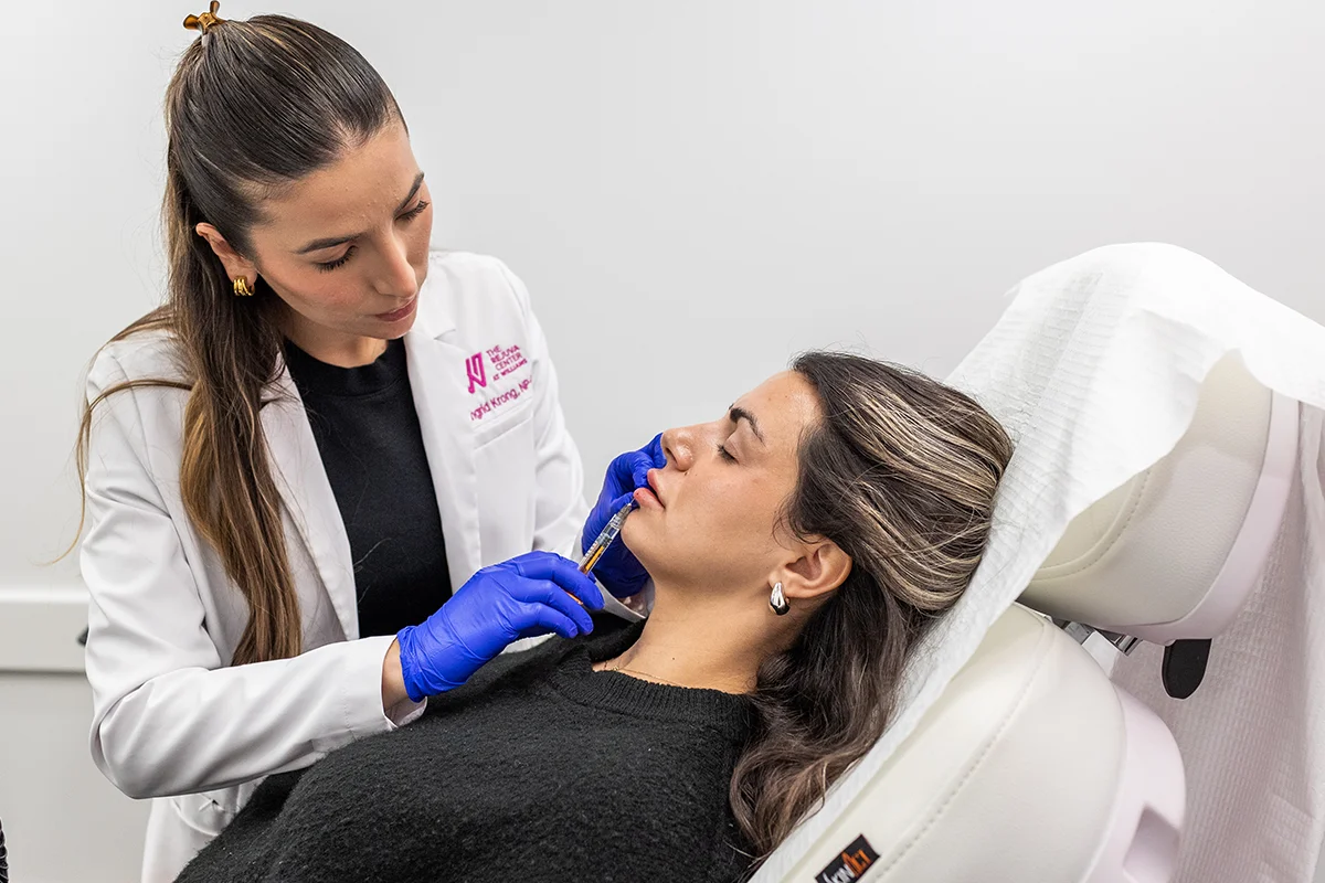 Young woman receiving injectable dermal filler in her bottom lip for balanced, natural-looking volume.