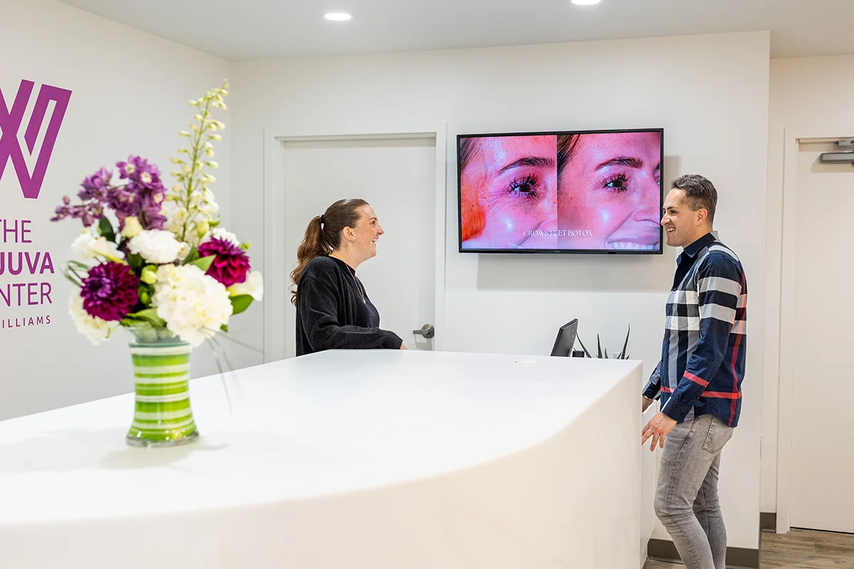 Middle-aged man talking and laughing with front desk manager at Rejuva Center in Saratoga Springs, NY. 