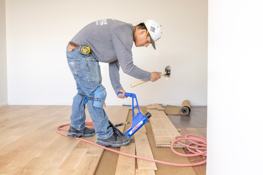 Professional flooring installer securing hardwood planks with a flooring nailer during installation.