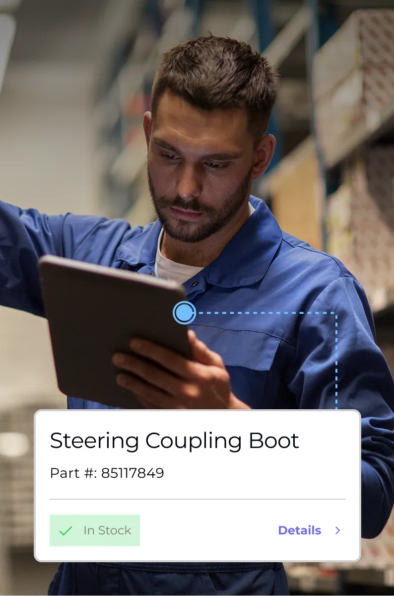 Man in blue work uniform using a digital tablet in a warehouse with inventory labeled as 'Steering Coupling Boot, Part #: 85117849, In Stock'.
