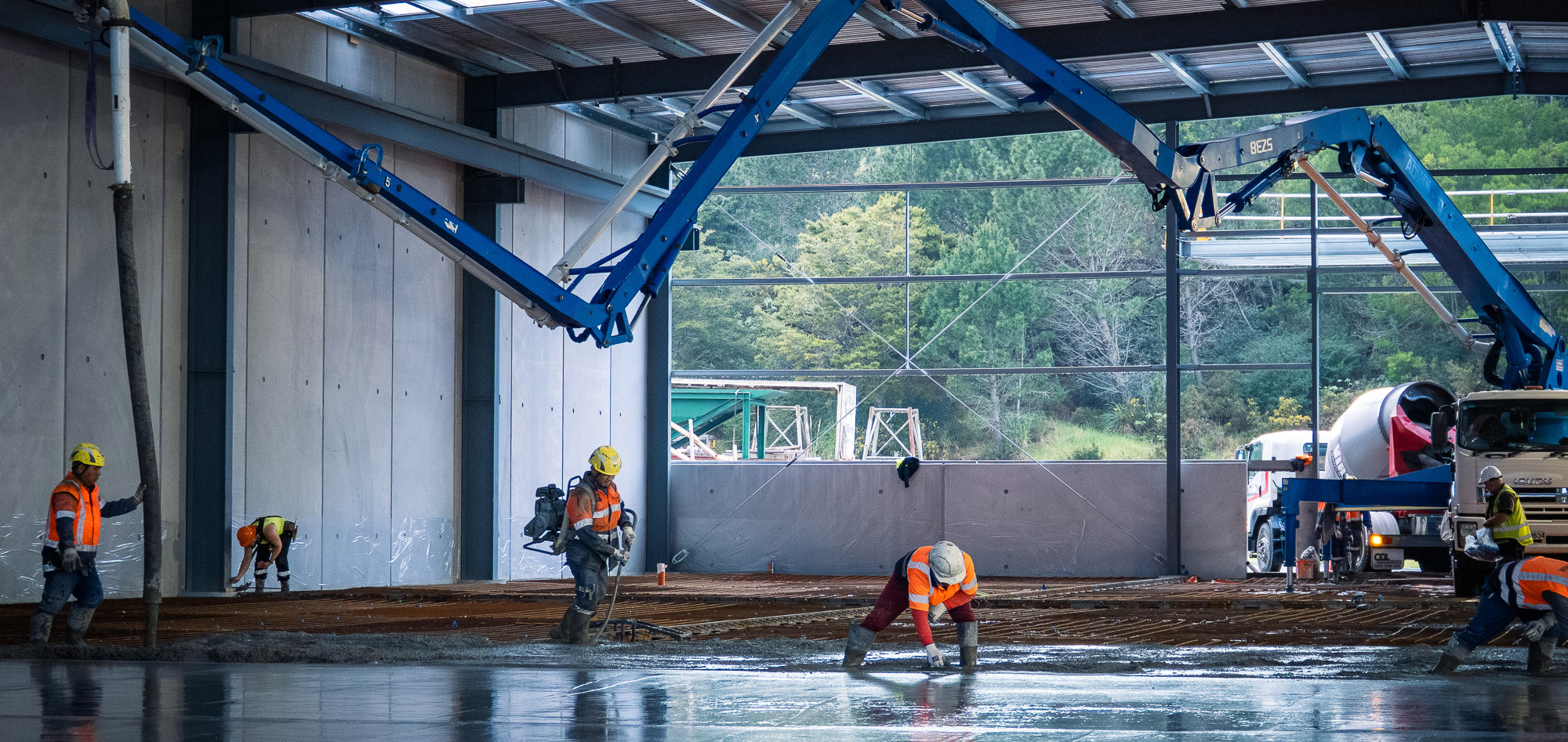 Advanced Concrete Pumping crew pouring and finishing a large warehouse floor with a blue placing boom in Wellsford, New Zealand.