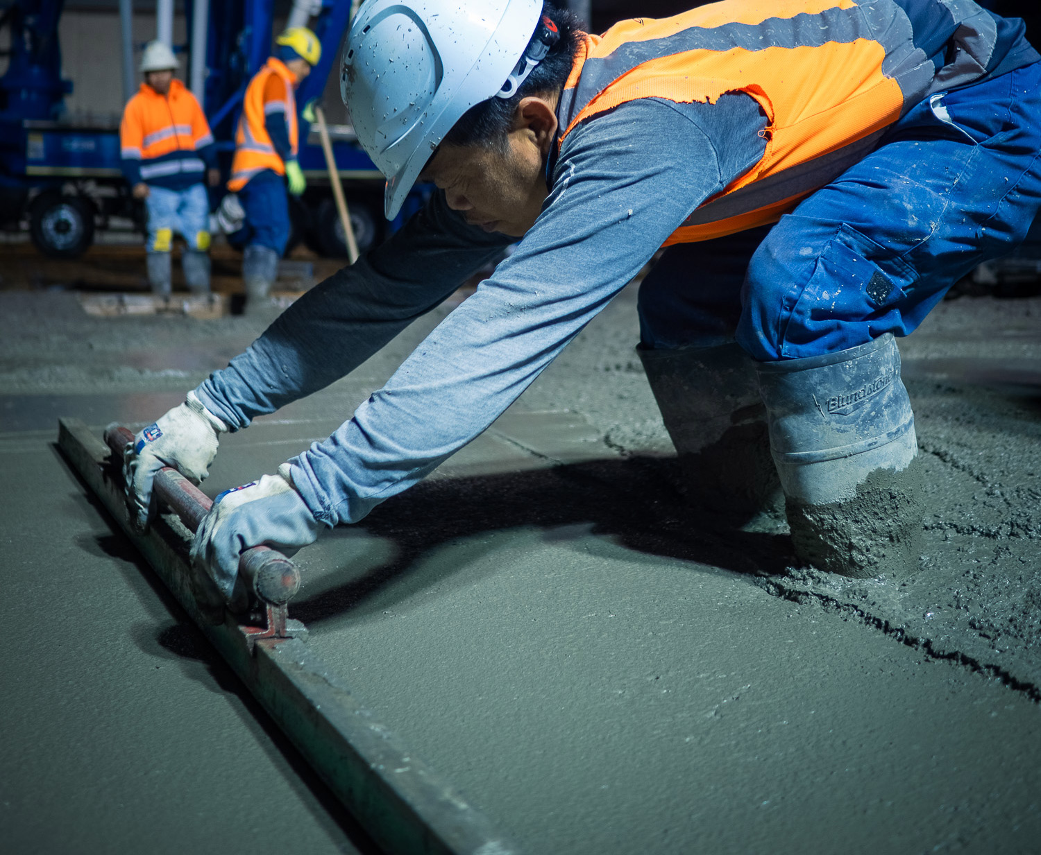 Advanced Concrete Pumping crew member levelling freshly poured concrete with a hand screed inside an industrial build, Wellsford, New Zealand.