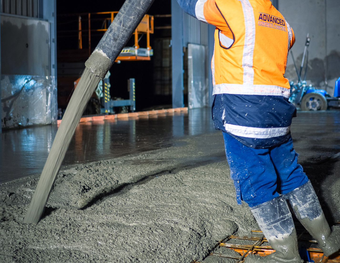 Advanced Concrete Pumping operator guiding a concrete pump hose as it pours onto reinforcing mesh for an indoor slab pour, Auckland, New Zealand.