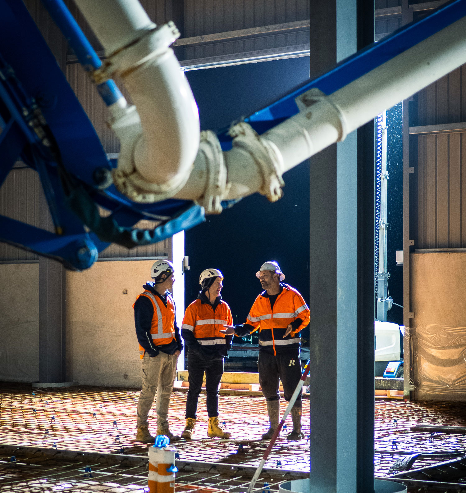 Advanced Concrete Pumping crew conferring beneath a placing boom on rebar during an indoor slab pour, Wellsford, New Zealand.