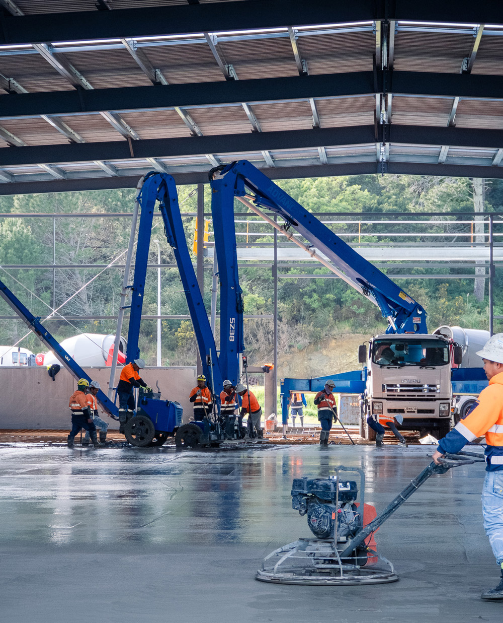 Advanced Concrete Pumping shotcrete setup at a warehouse build in Wellsford, New Zealand, with blue boom feeding inside and a branded ute in the foreground.