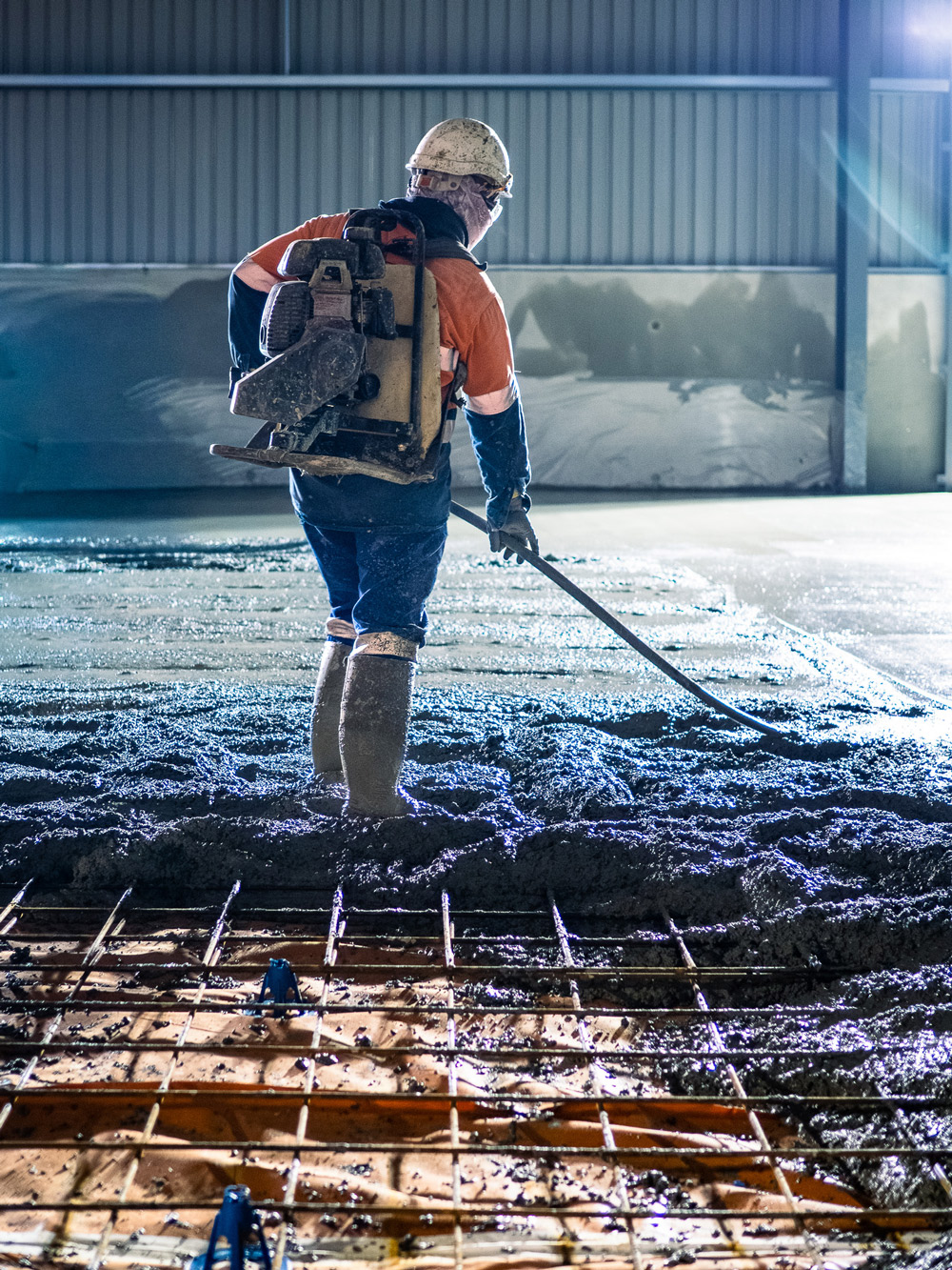 Worker laying and smoothing concrete floor inside warehouse construction site