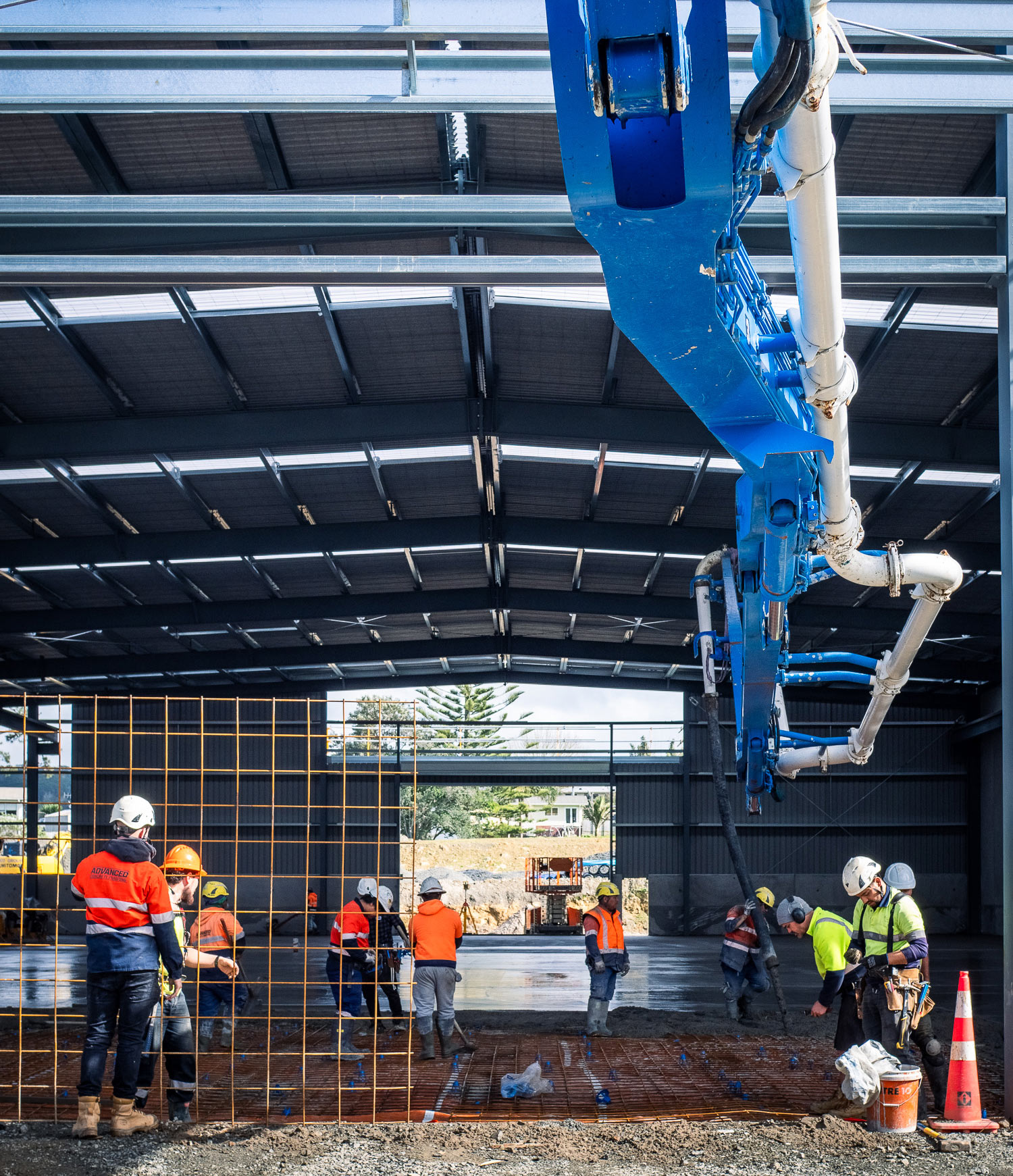 Construction worker in high-visibility gear operating concrete pumping equipment on a coastal building site in New Zealand.