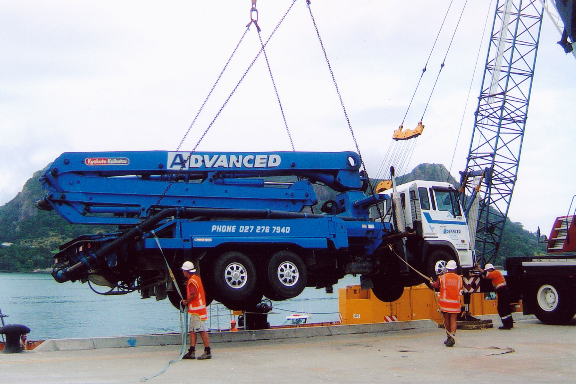 Advanced Concrete Pumping crew members standing beside a concrete boom pump truck on site.
