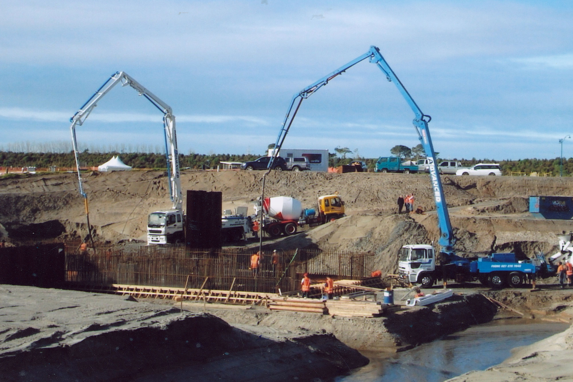 Two Advanced Concrete Pumping boom trucks working on a large excavation and concrete construction site.