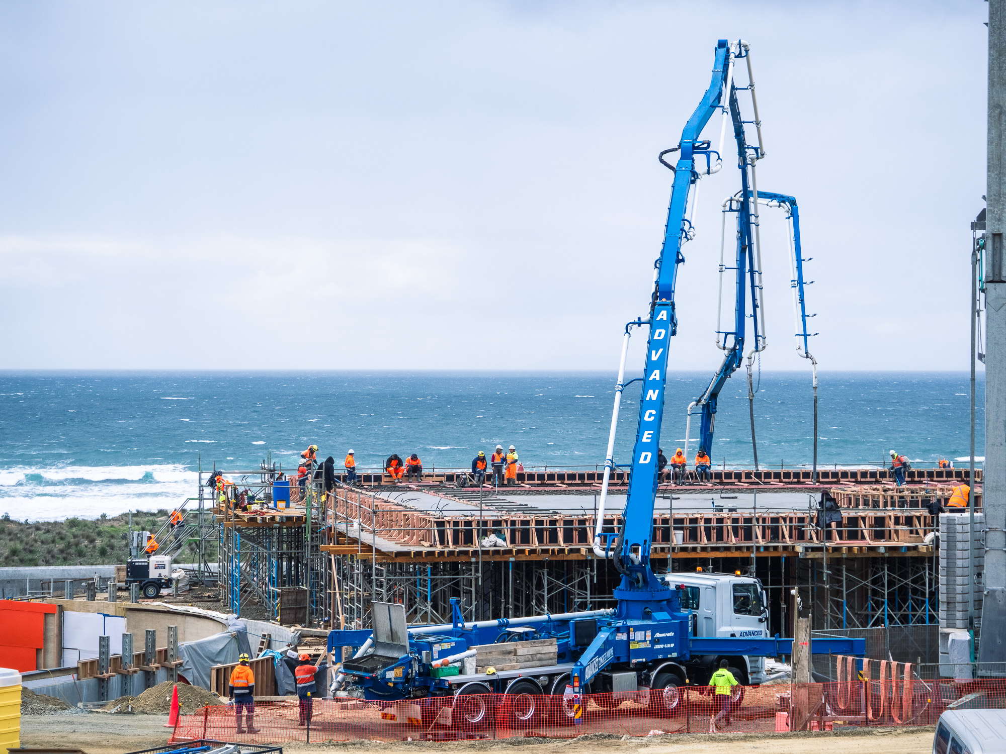 Advanced Concrete Pumping truck with extended blue boom arm pouring concrete at a construction site with scaffolding and formwork.