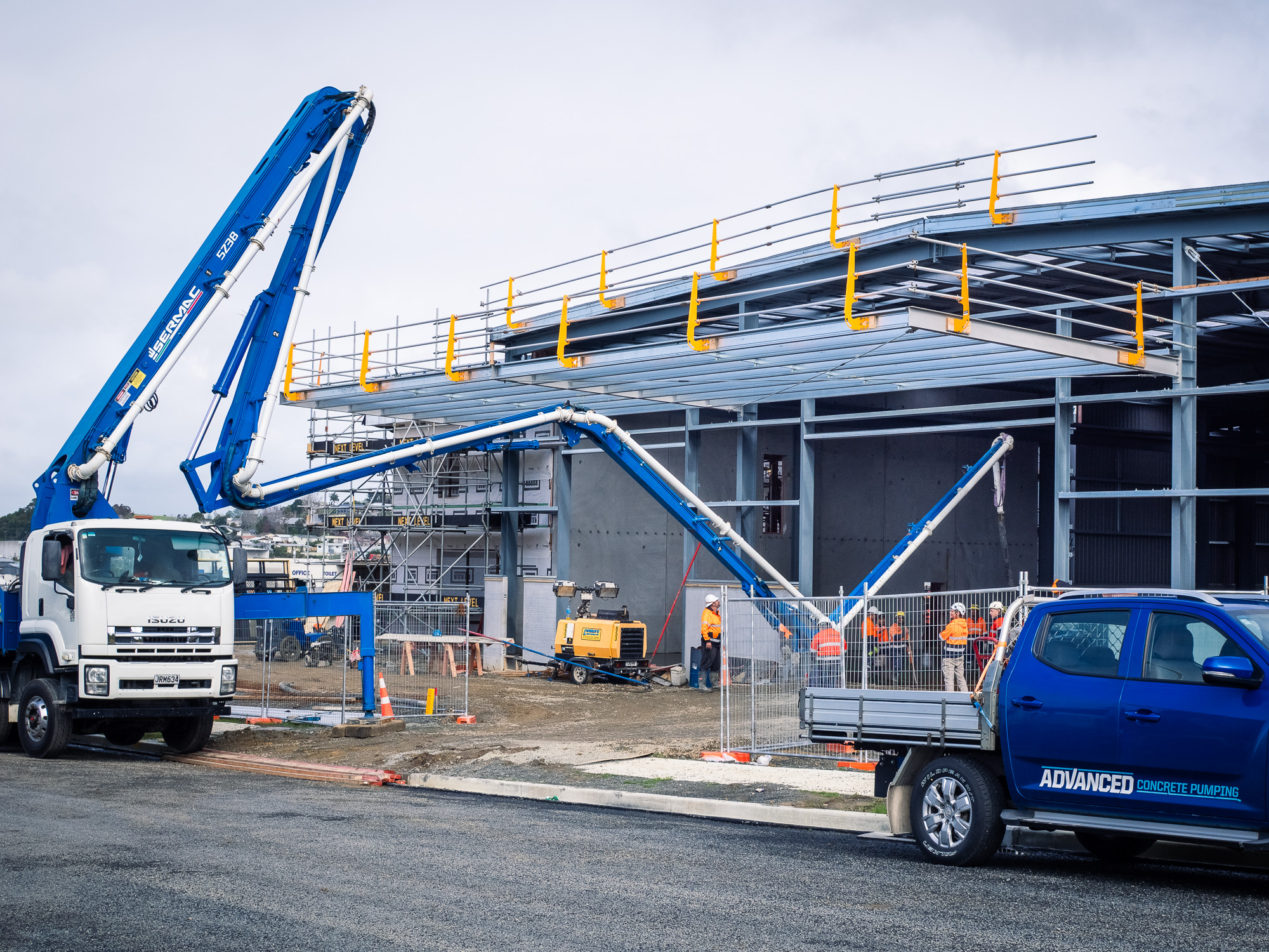 Construction worker in high-visibility gear operating concrete pumping equipment on a coastal building site in New Zealand.