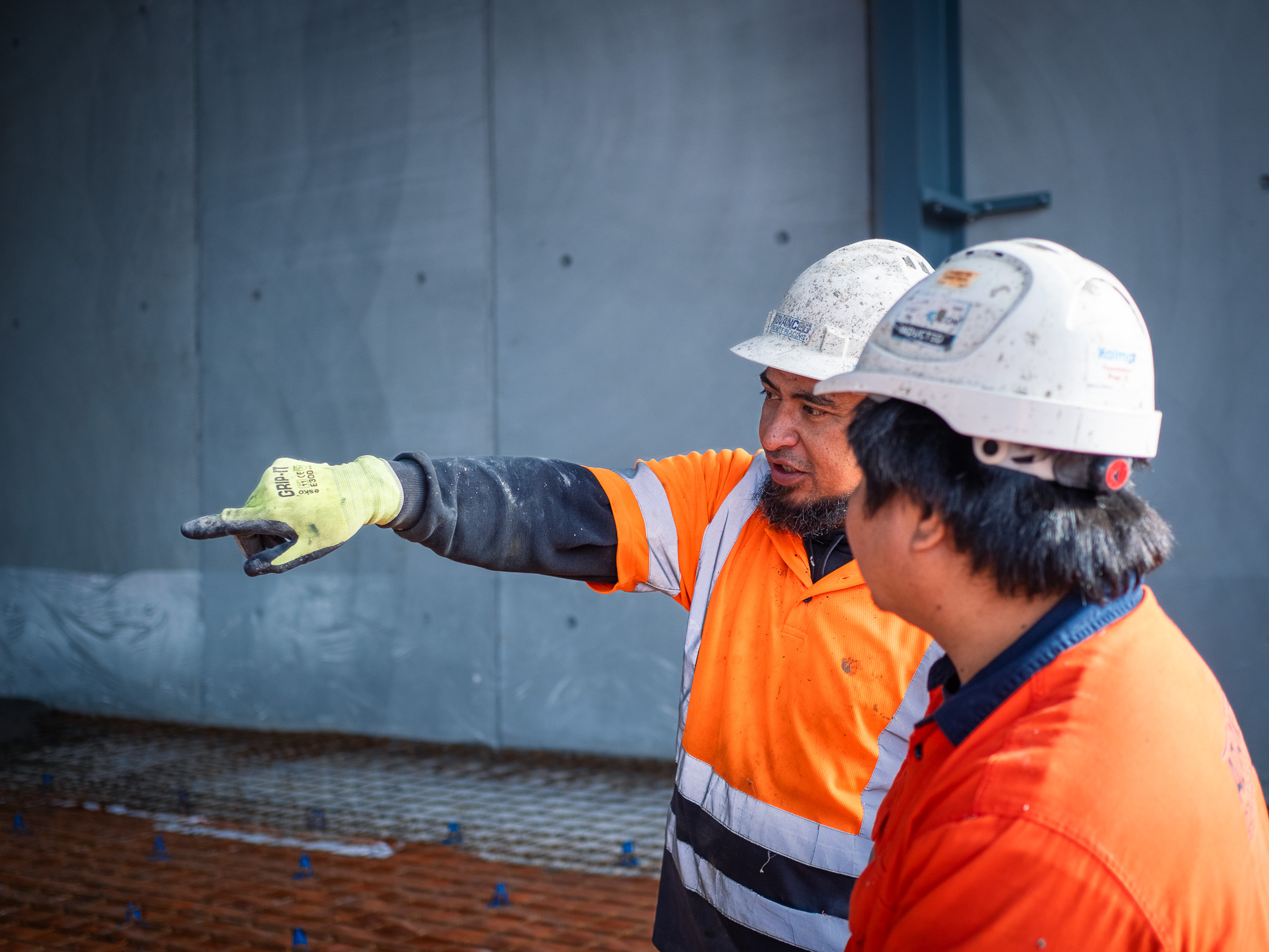 Construction worker in high-visibility gear operating concrete pumping equipment on a coastal building site in New Zealand.