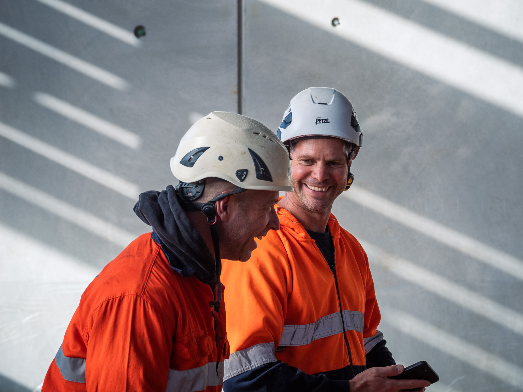 Construction worker in high-visibility gear operating concrete pumping equipment on a coastal building site in New Zealand.