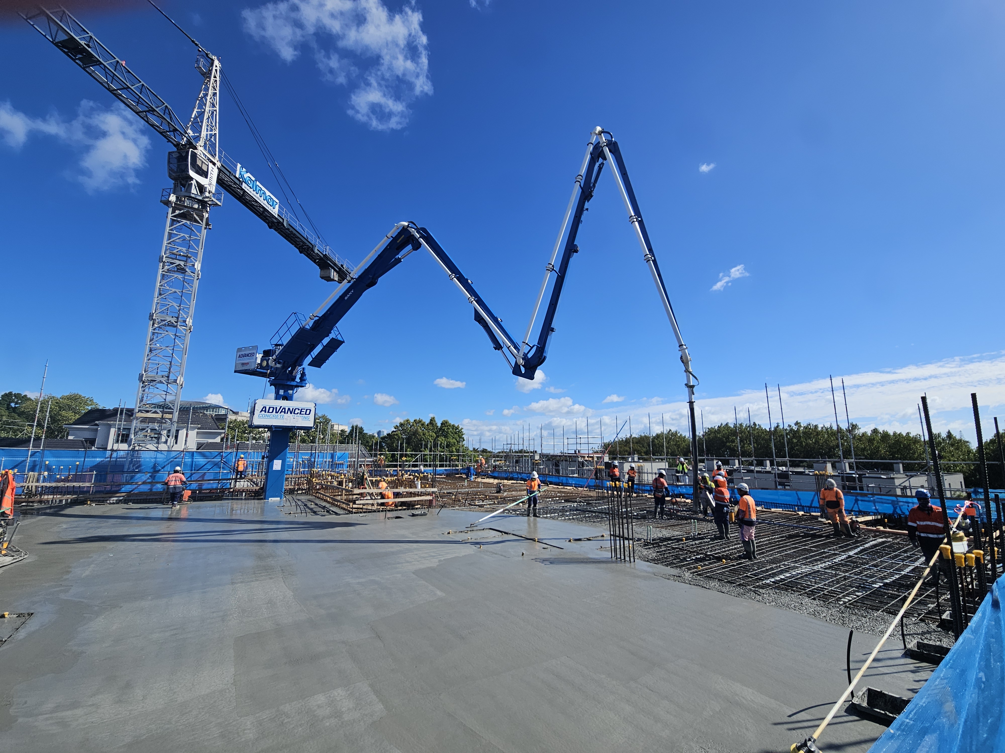 Construction worker in high-visibility gear operating concrete pumping equipment on a coastal building site in New Zealand.