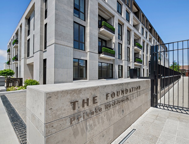 Exterior view of The Foundation Private Residences showing the front gate, stone façade, and building signage.