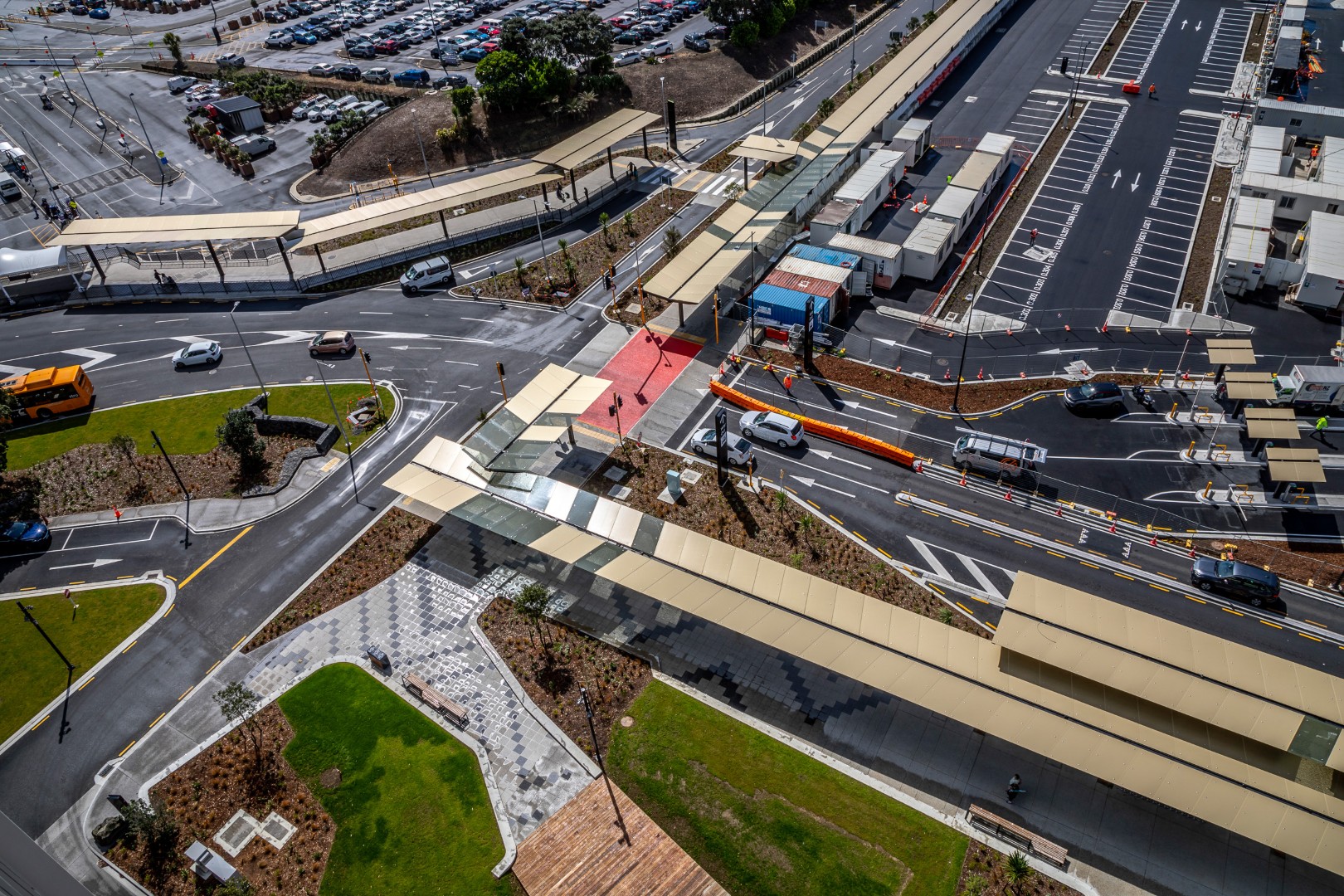Aerial view of new transport hub with covered pedestrian walkways, landscaped areas, and surrounding road network with cars and buses.
