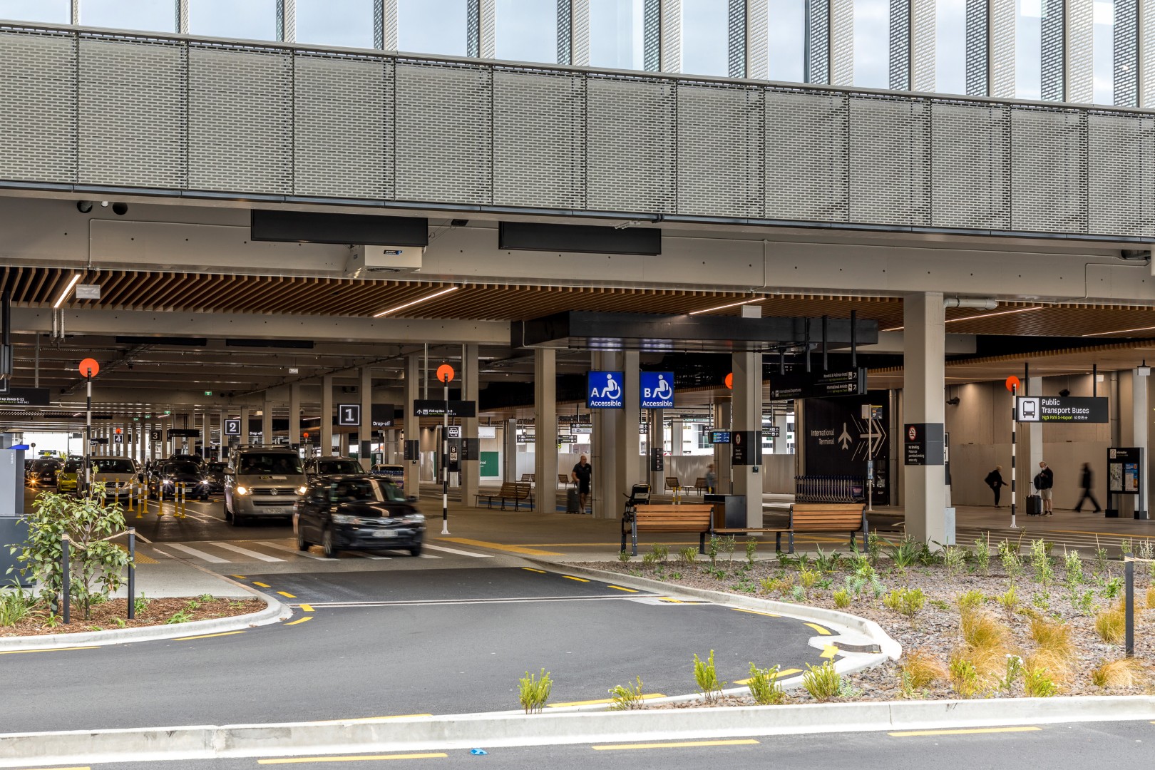Modern multi-level car park and transport facility with vehicles arriving at the drop-off zone under a covered walkway.
