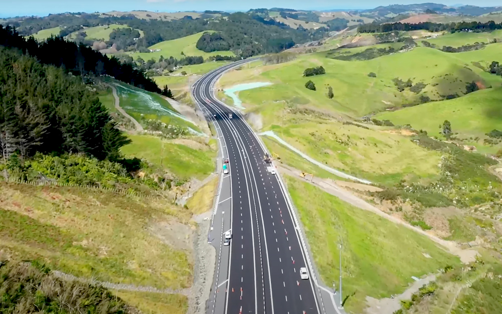 Elevated view of the Ara Tūhono – Pūhoi to Warkworth motorway winding through green valleys and native bush, featuring newly constructed dual carriageways.